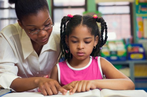 Teacher helping young girl with cut-out alphabet letters