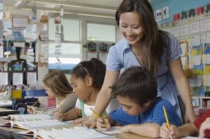 A teacher in the classroom helping children to do the task.